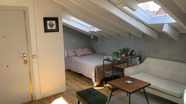 A loft-style bedroom with a skylight, a bed, a sofa, and a small table. - Studio Centro Madrid (Madrid)