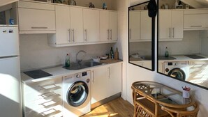 A compact kitchen with white cabinets, a washing machine, a sink, and a mirror reflecting the kitchen. - Studio Centro Madrid (Madrid)