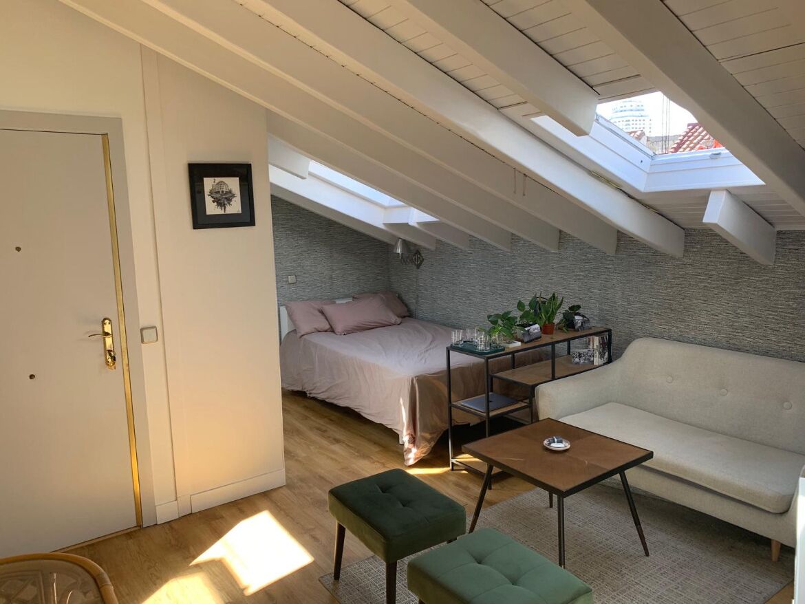 Un dormitorio tipo loft con tragaluz, cama, sofá y una pequeña mesa.