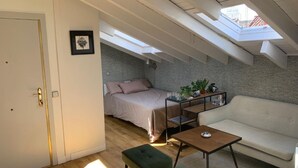 A loft-style bedroom with a skylight, a bed, a sofa, and a small table. - Studio Centro Madrid (Madrid)