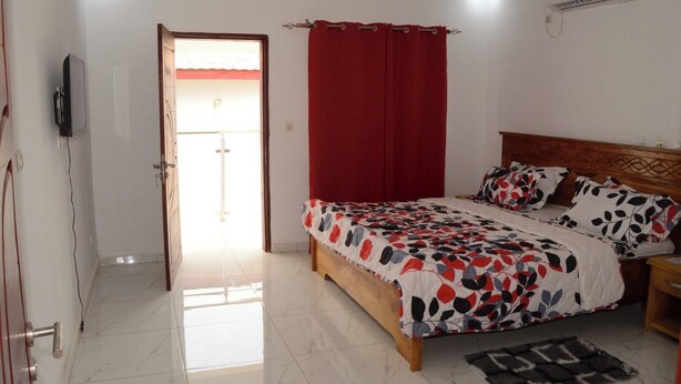 A bedroom with a bed, a TV, a red curtain, and a ceiling fan. - Hotel Labertina (Yamoussoukro)