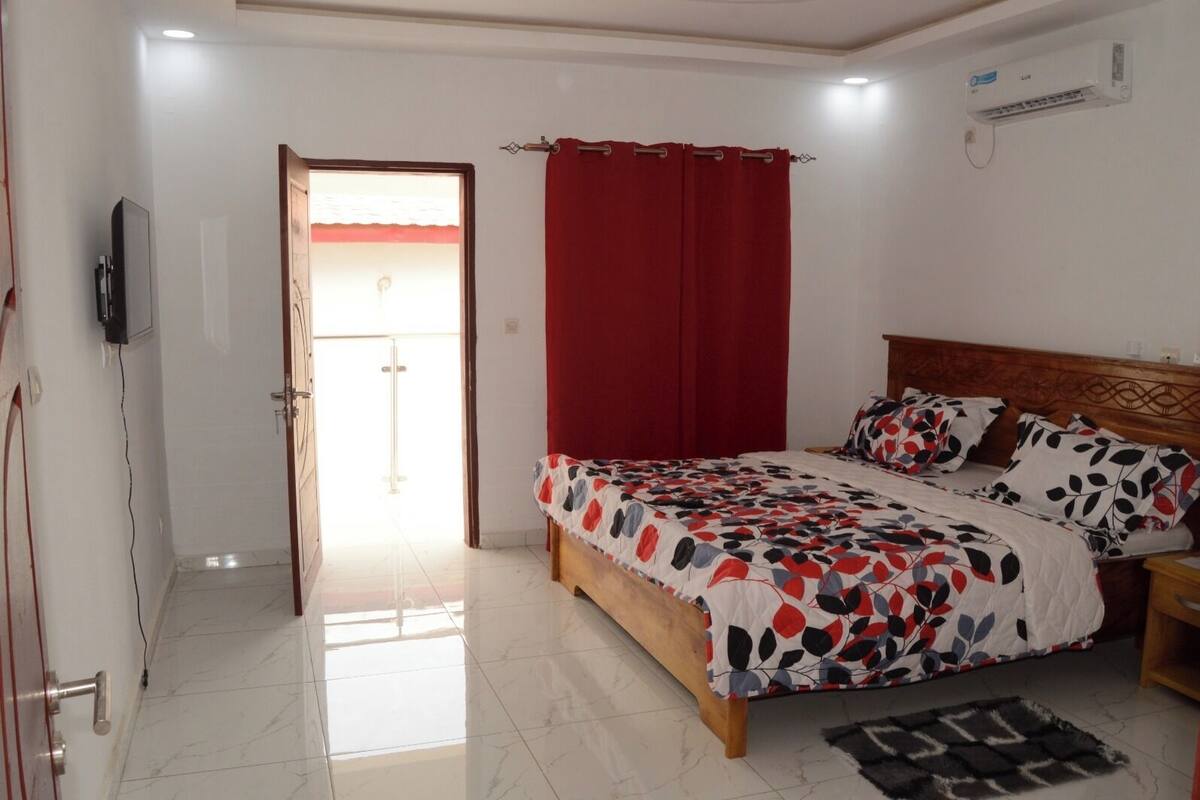 A bedroom with a bed, a TV, a red curtain, and a ceiling fan.