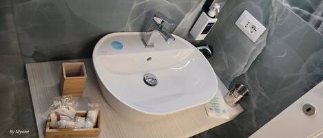 Kylpyhuone, jossa on valkoinen pesuallas, peili, saippua-annostelija ja pieni puinen alusta, jossa on hygieniatuotteita.