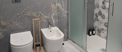 Un baño moderno con inodoro, bidé y ducha con mampara de vidrio.