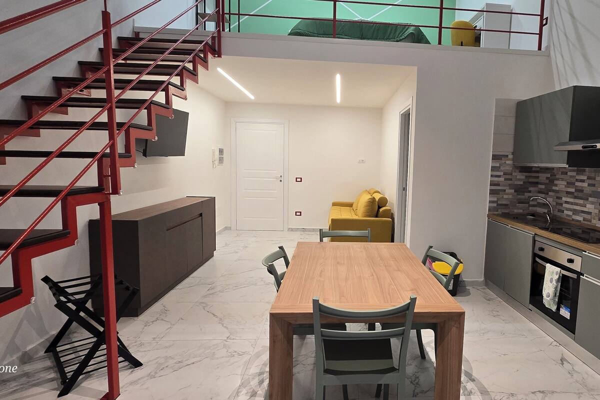 Une cuisine moderne avec un coin repas, un escalier et une porte donnant sur une autre pièce.