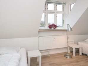 A bedroom with a sloped ceiling, a window with a view, a radiator, a bedside table, a lamp, and a bed.