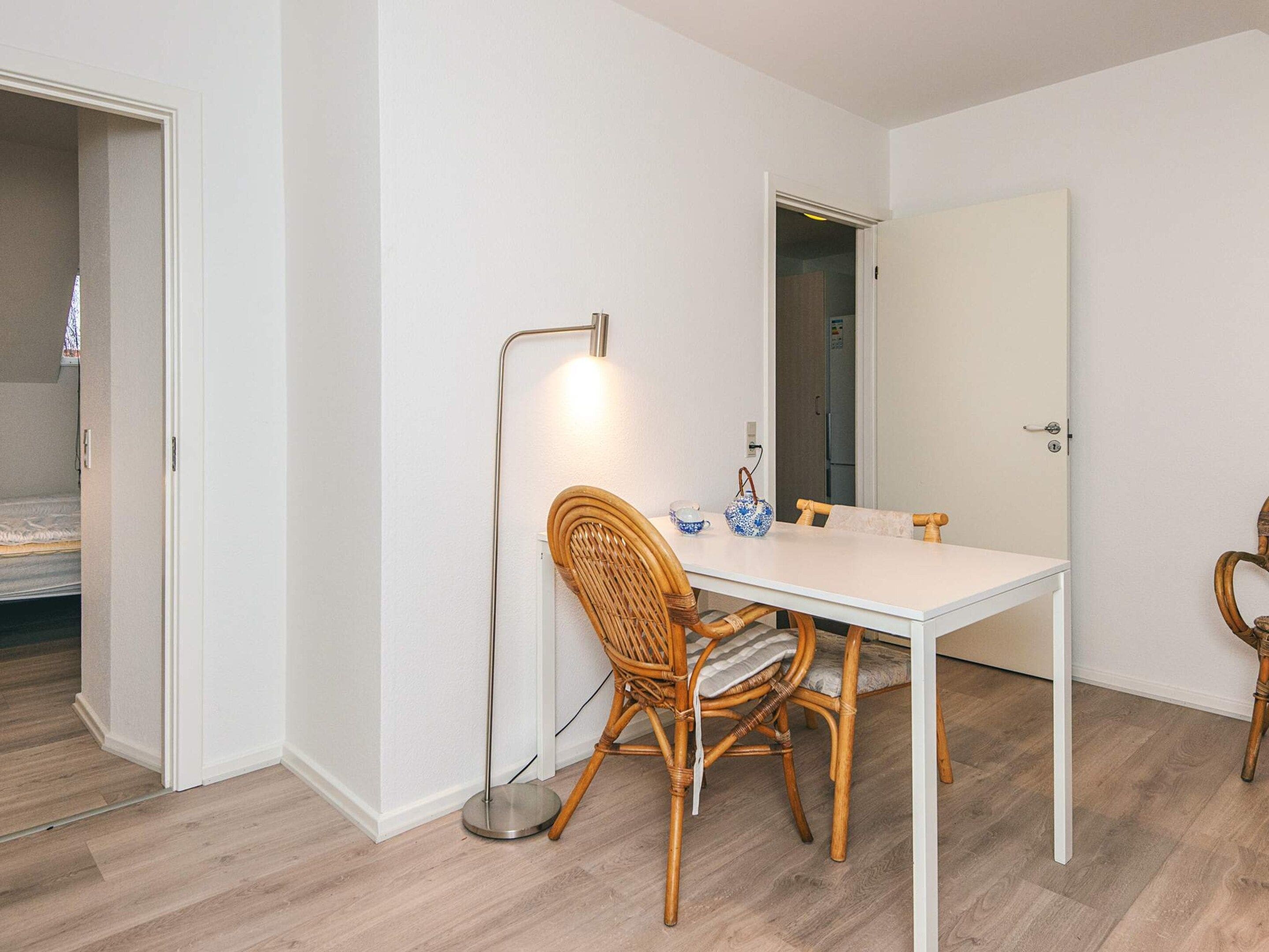 A room with a white table, wicker chairs, a floor lamp, and a door leading to a closet.