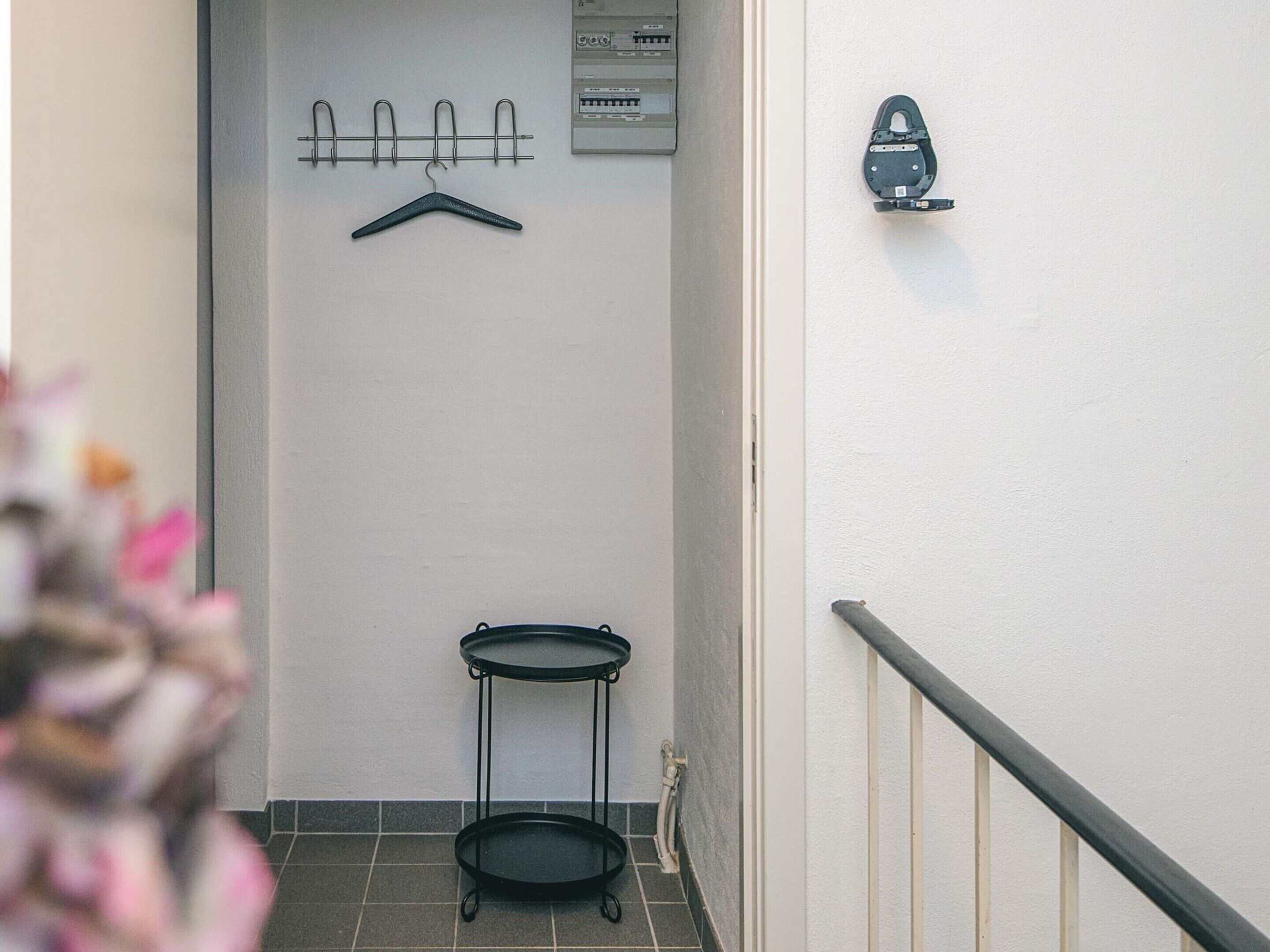 A narrow hallway with a coat rack, a small table, and a wall-mounted device.