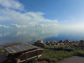 A calm lake with a wooden bench and picnic table in the foreground, surrounded by rocks and grass.