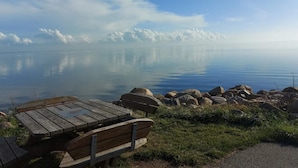 A calm lake with a wooden bench and picnic table in the foreground, surrounded by rocks and grass.