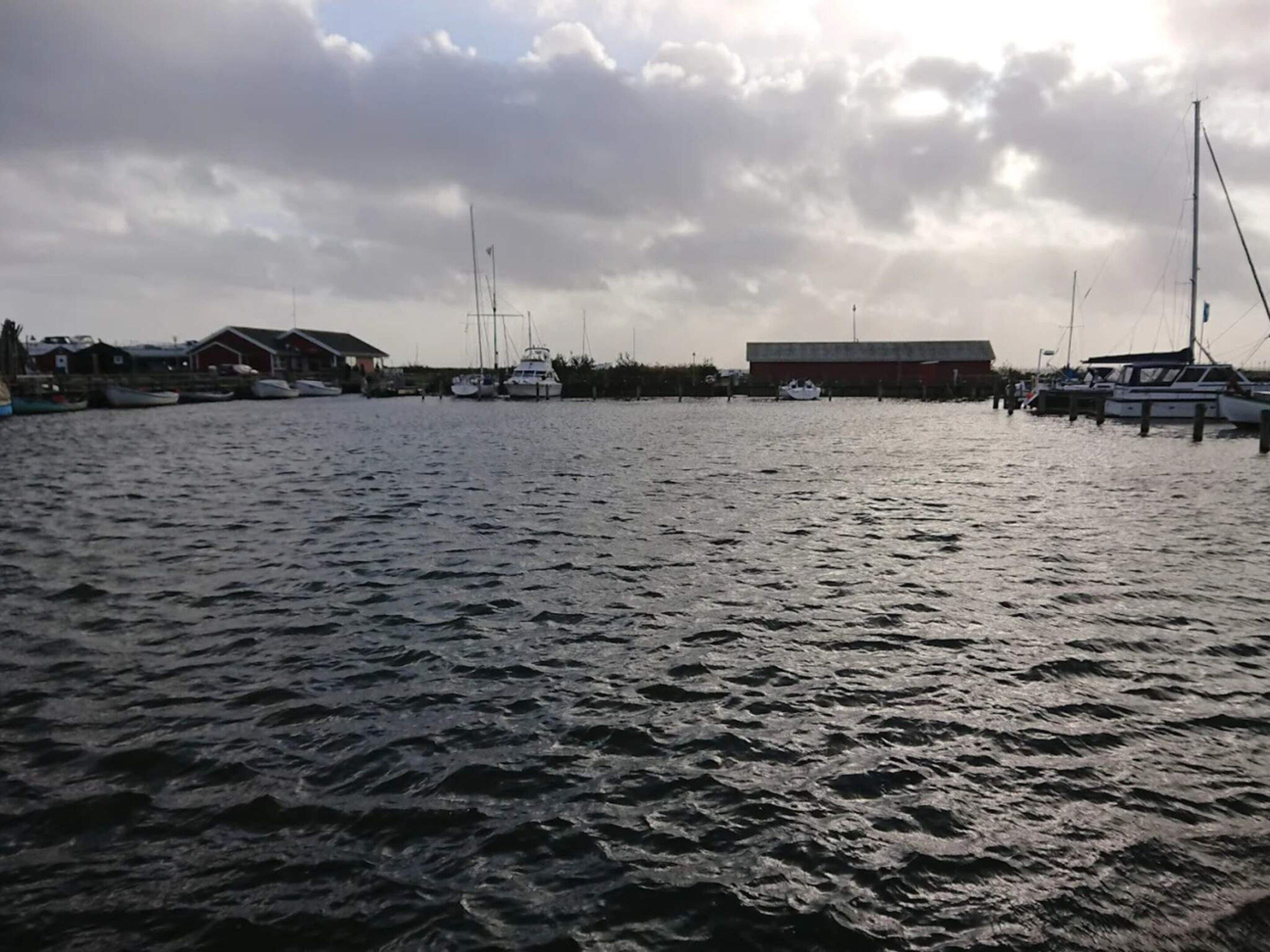 A marina with boats docked, a building with a red roof, and a cloudy sky.