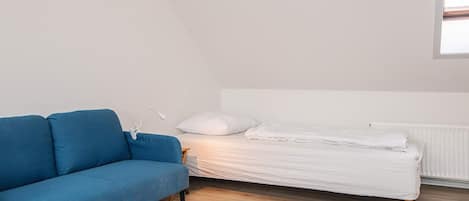 A room with a blue sofa, a white bed with a white mattress and pillows, and a white radiator.