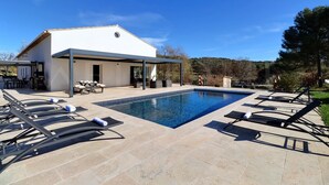 Un área de piscina moderna al aire libre con sillones de descanso y un patio cubierto.
