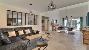 Amplia sala de estar con sofá, mesa de centro y mesa de comedor. Hay lámparas colgantes y un espejo grande en la pared.