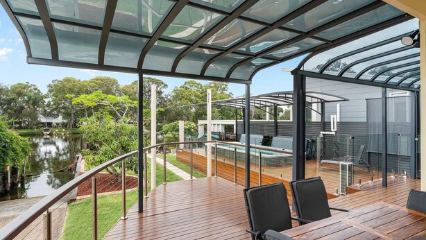 Une terrasse extérieure couverte avec une piscine, un plancher en bois et des rampes en verre.