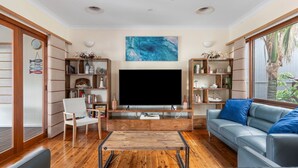 Un salon doté d’un grand téléviseur à écran plat, d’un parquet, d’un canapé bleu et d’étagères en bois remplies de livres et d’objets décoratifs.
