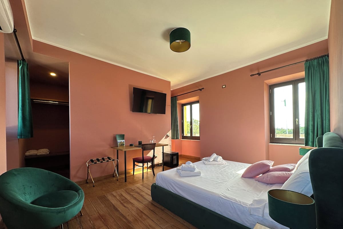Ein Hotelzimmer mit Bett, Schreibtisch, Stuhl, Fernseher und einem Fenster mit Vorhängen.