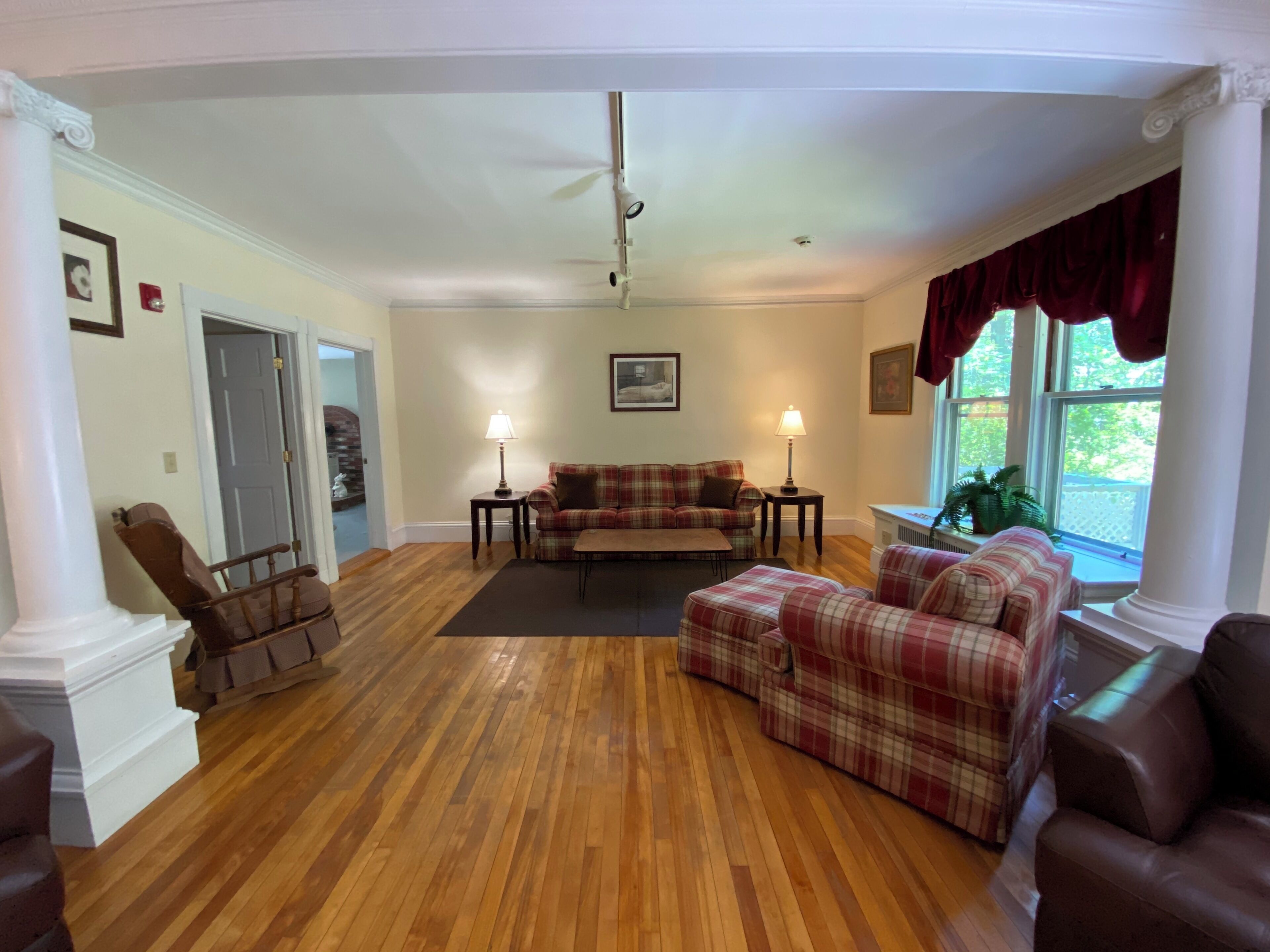 A spacious living room with hardwood flooring, a plaid sofa set, a wooden chair, and a fireplace.