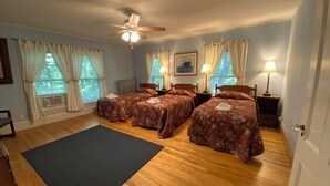 Una habitación con cuatro camas, ventilador de techo y ventanas grandes con cortinas.