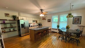 Una cocina con una isla central, piso de madera y un comedor con mesa y sillas.