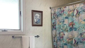 Un baño con inodoro, lavamanos, cortina de ducha con motivos de peces, un estante pequeño y un cuadro en la pared.