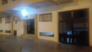 A building exterior with a staircase leading to a door, a large window with metal bars, and a bright light source above.