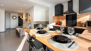 Eine moderne Küche mit schwarzen Schränken, einem Holzespeisetisch gedeckt mit Tellern und Gläsern, und ein graues Sofa im Wohnbereich.