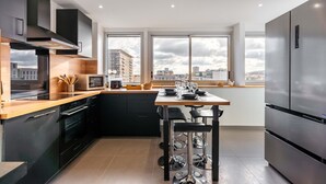 Eine moderne Küche mit schwarzen Schränken, Edelstahlgeräten, einer Holzarbeitsplatte und großen Fenstern mit Blick auf die Stadt.