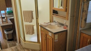 Een kleine badkamer in een camper, met een douchecabine, een wastafelmeubel en een spiegel.