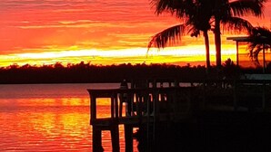 Een zonsondergang boven het water, met palmbomen en een steiger.