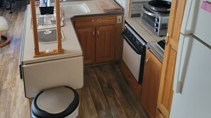 Een kleine keuken met houten kastjes, een magnetron, een broodrooster en een koelkast.