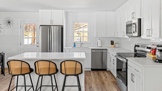 A modern kitchen with white cabinets, stainless steel appliances, and a central island with bar stools. - 3-bedroom house in by downtown Durham NC (Durham)
