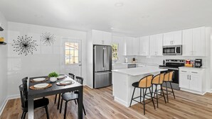 A modern kitchen with white cabinets, stainless steel appliances, and a wooden dining table with chairs. - 3-bedroom house in by downtown Durham NC (Durham)