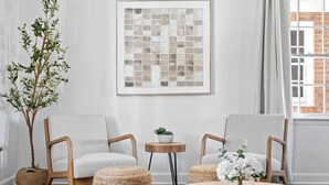 A modern living room with two grey upholstered chairs, a round wooden coffee table, and a woven pouf. A large abstract artwork is on the wall, and a potted plant is in the corner. - 3-bedroom house in by downtown Durham NC (Durham)