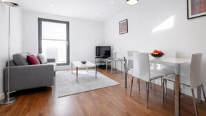 Ein modernes Wohnzimmer mit grauem Sofa, Couchtisch, Fernseher und Essbereich mit weißem Tisch und Stühlen.