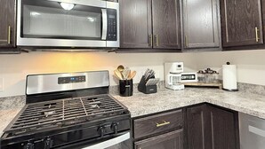 A kitchen with dark wood cabinets, a stainless steel microwave, a gas stove, a coffee maker, and a set of knives.