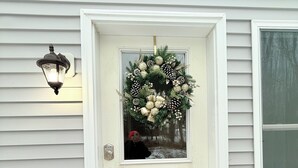 A white front door with a wreath, a wooden bench, and a wall-mounted light fixture.