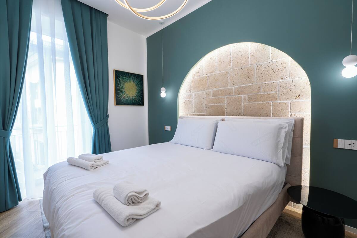 A neatly made bed with white linens and towels, a brick-patterned headboard, and a modern light fixture.