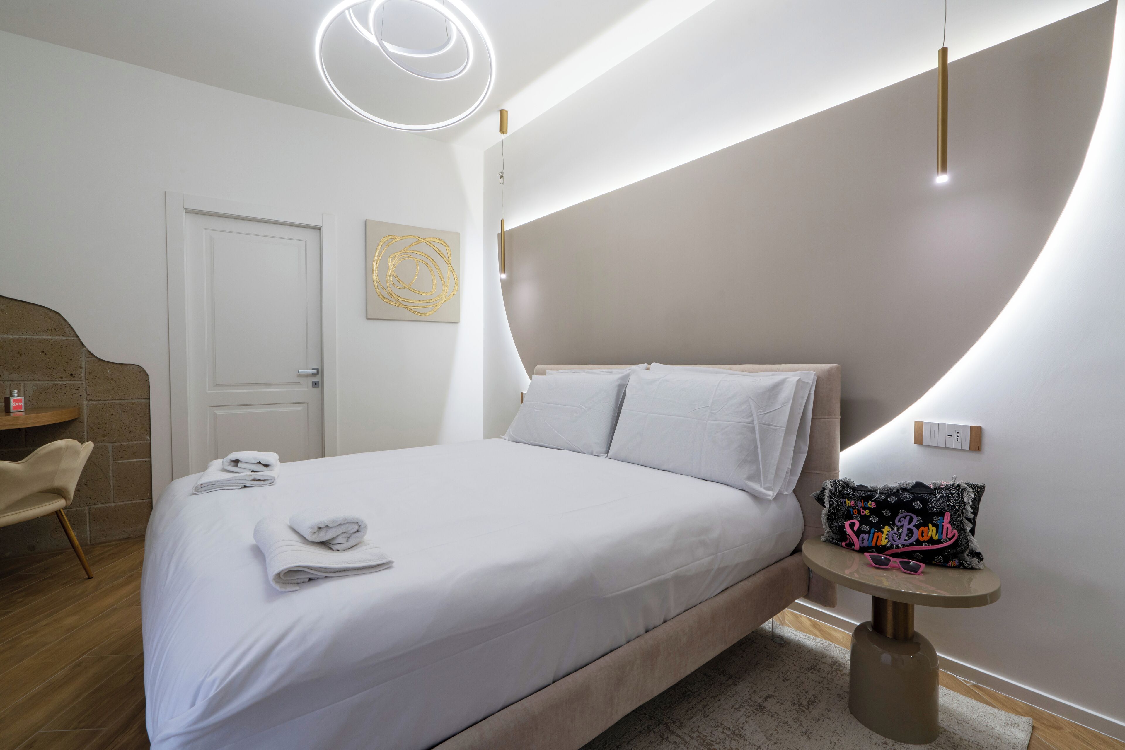 A modern bedroom with a bed, a bedside table, a chair, and a wall-mounted light fixture.