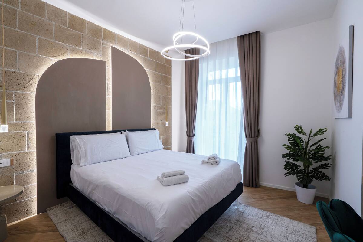 A modern bedroom with a brick wall, a large bed, a potted plant, and a view of the outdoors.