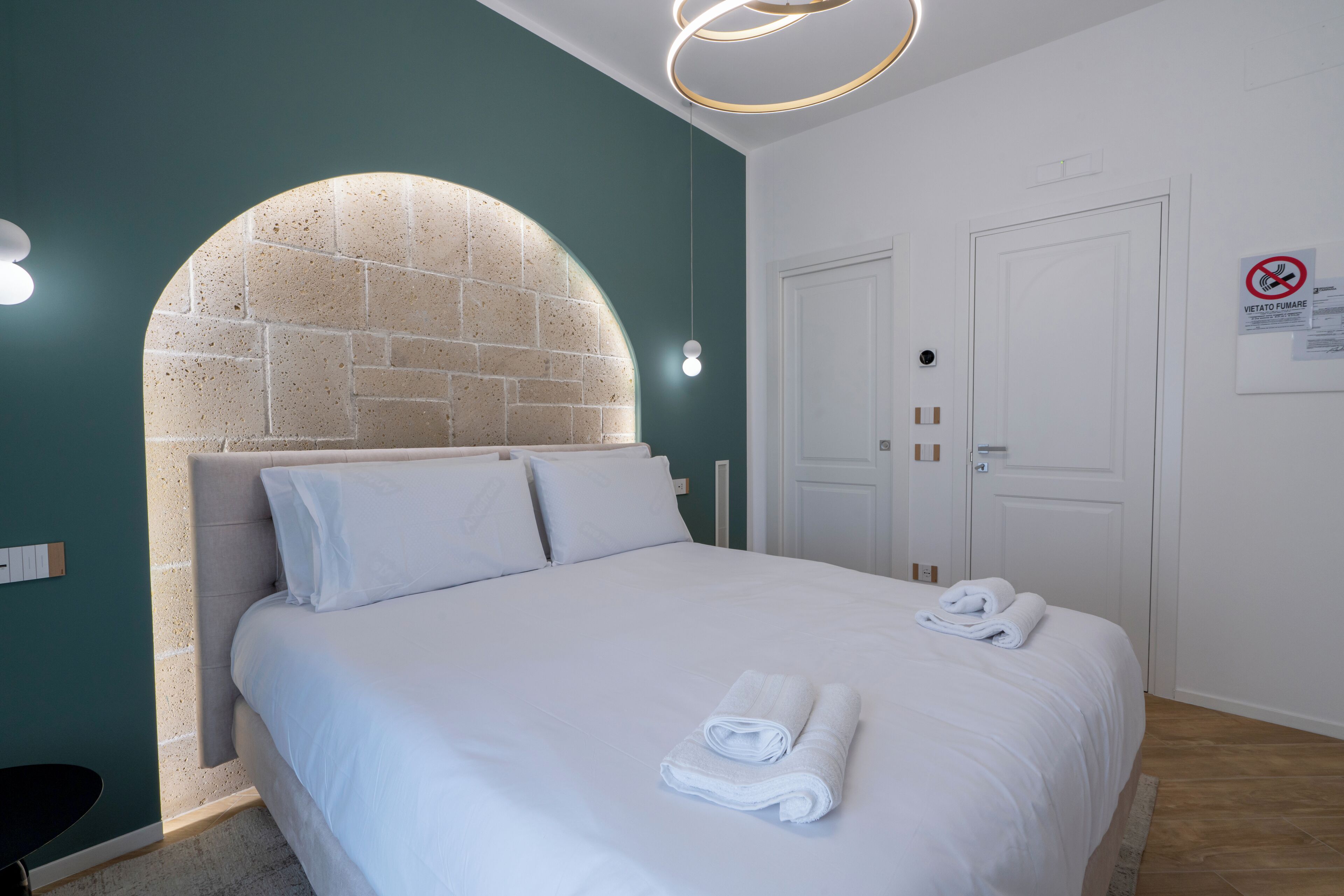 A neatly made bed with white linens and towels, a brick-patterned headboard, and a circular light fixture above it.