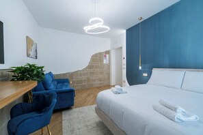 Une chambre d’hôtel moderne avec un grand lit, un bureau avec une chaise, un canapé bleu et une plante en pot.