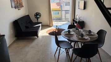 Een moderne woonkamer met een bank, eettafel, stoelen en een ventilator.