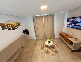 Una sala de estar con un sofá, una mesa redonda con una pequeña estatua, un televisor y un ventilador.