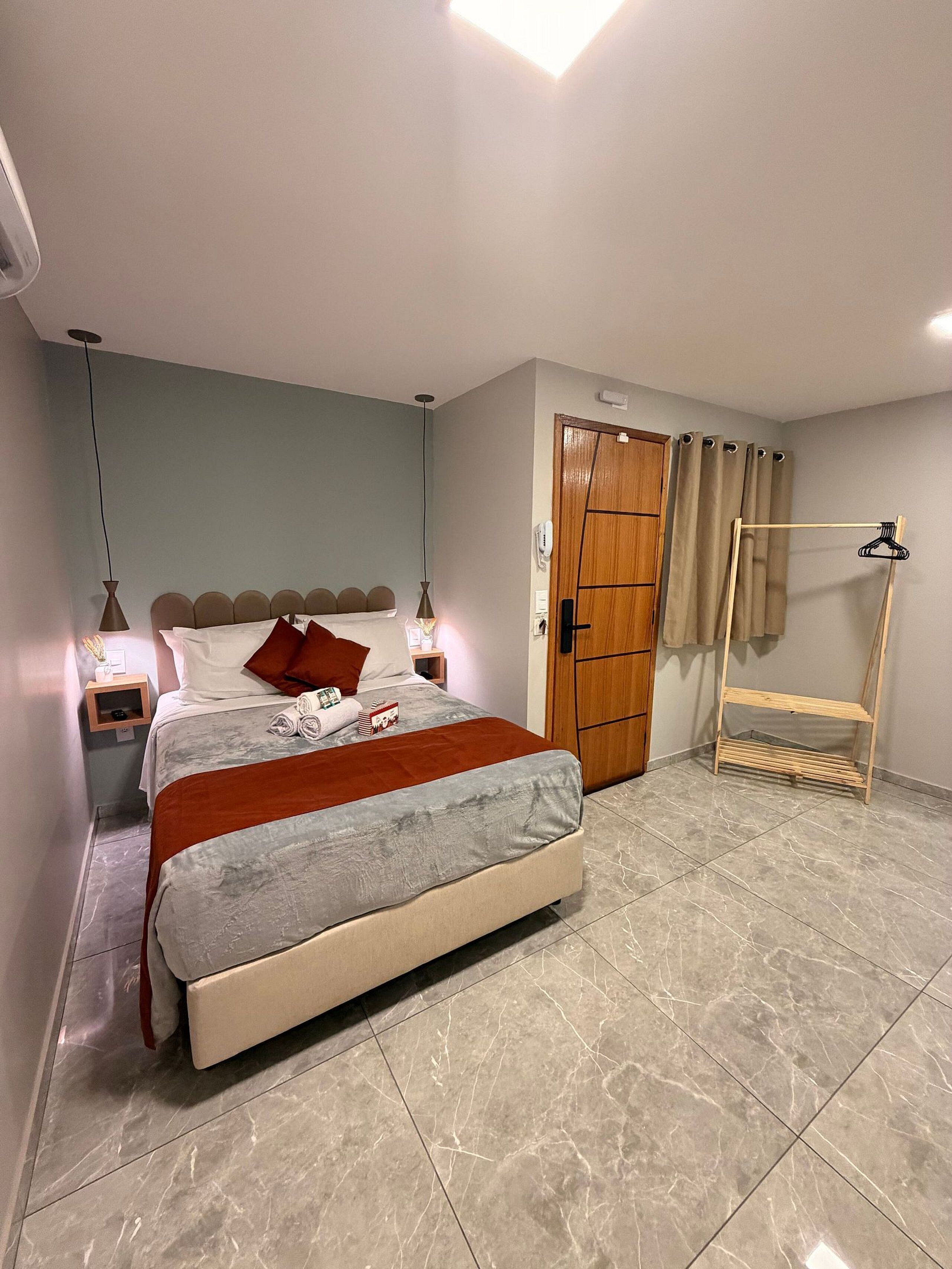 A bedroom with a bed, bedside tables, a wardrobe, a hanging rack, and a tiled floor.