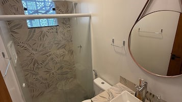 Casa de banho com cabine de duche em vidro, sanita, lavatório com espelho e azulejos estampados.