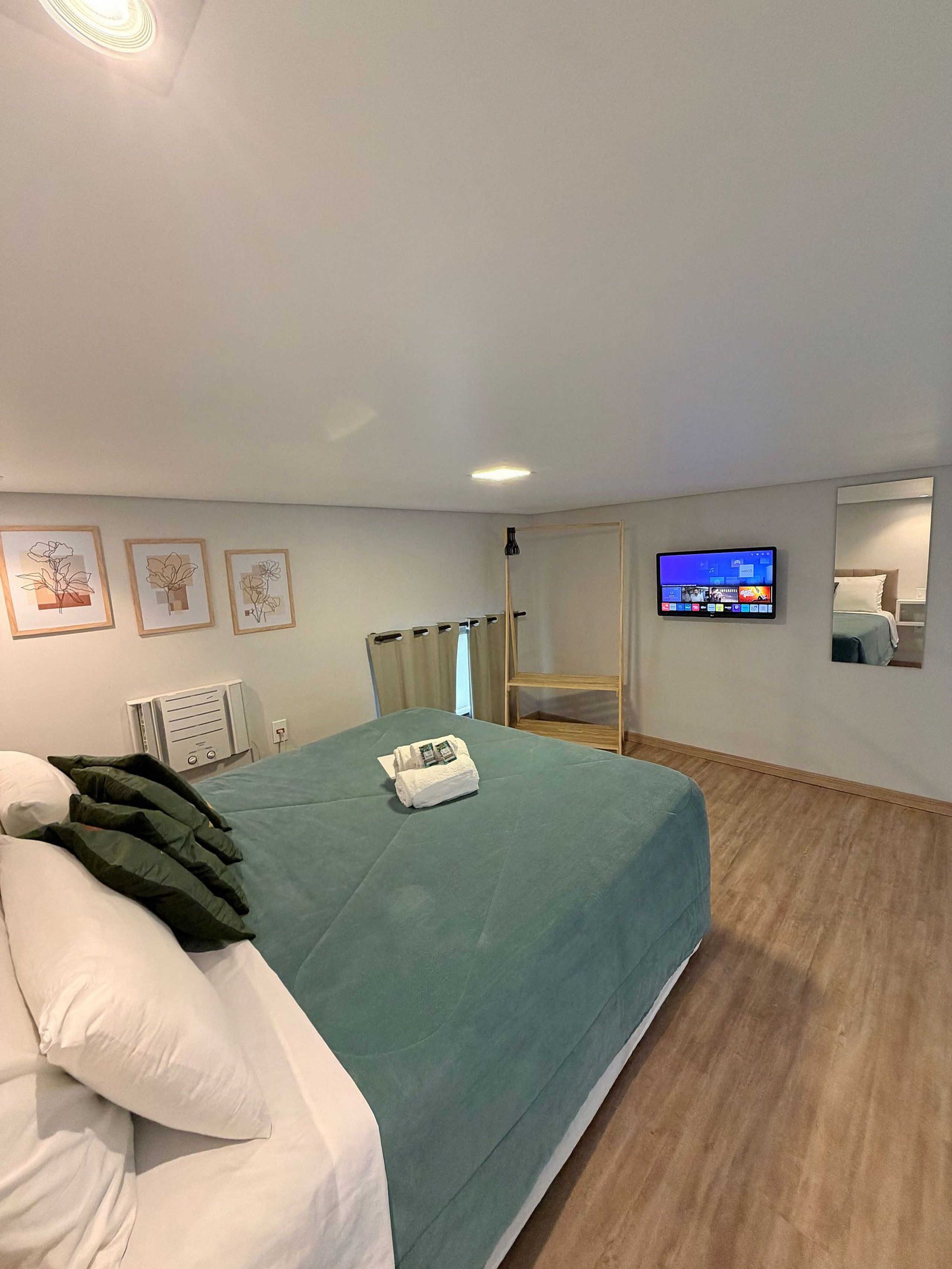 A hotel room with a bed, a TV, a mirror, and artwork on the wall.