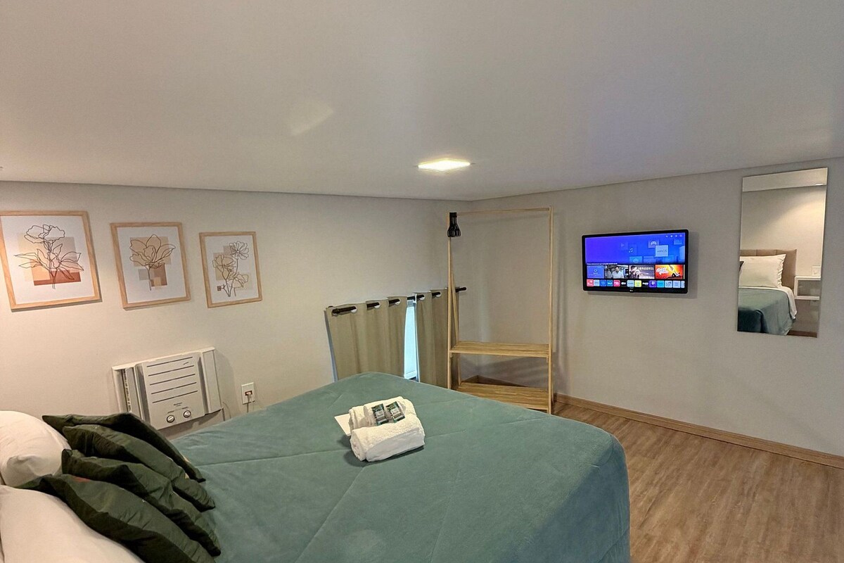 A hotel room with a bed, a TV, a mirror, and artwork on the wall.