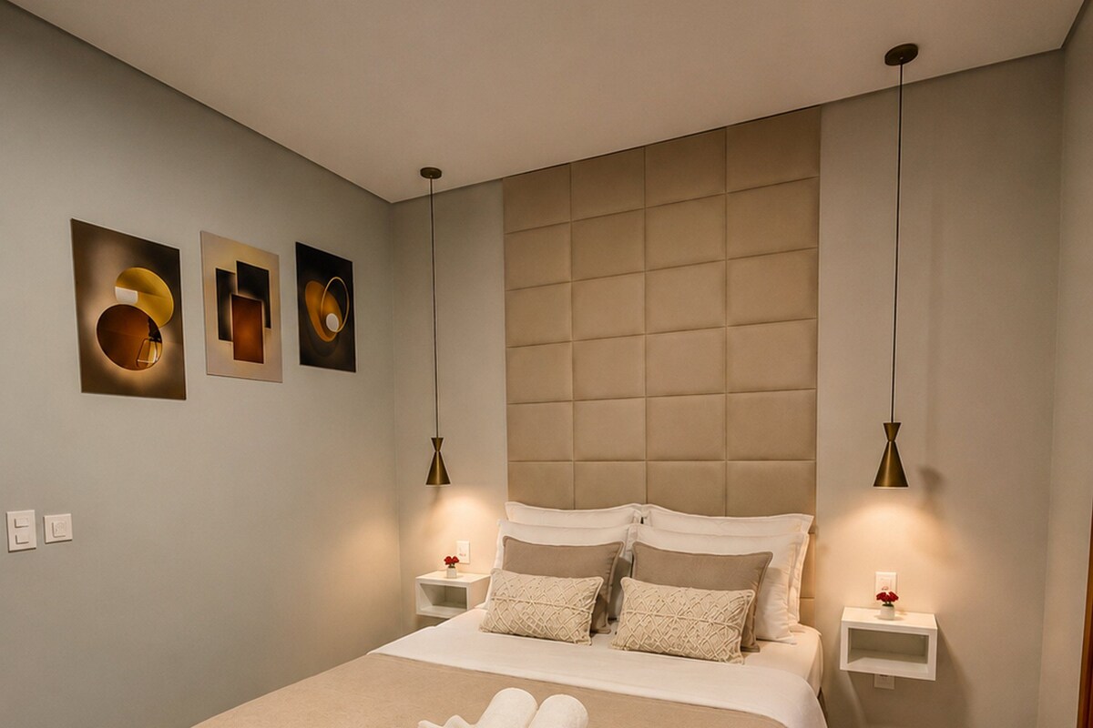 A hotel room with a large bed, two bedside tables, a headboard, and wall-mounted artwork.