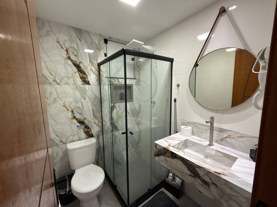 A bathroom with a glass-enclosed shower, a toilet, a sink with a marble countertop, and a round mirror.